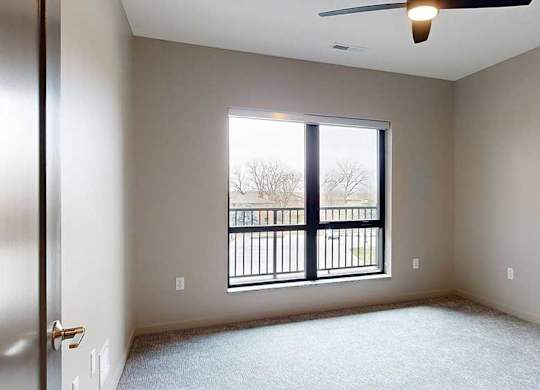 a bedroom with a ceiling fan and a large window overlooking a balcony