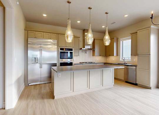 A gourmet kitchen with an oversized island, taupe wooden cabinetry, stainless steel commercial appliances, quartz countertops, a range hood, a tile backsplash, and pendant lighting.