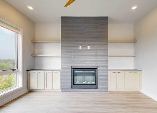 A modern living room with a fire place in a floor-to-ceiling mantel, and built-in cabinetry and shelves on either side.