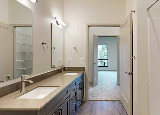 a bathroom with a double sink, mirror, and a door leading to a walk-through closet