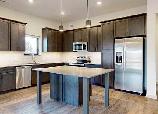 a modern L-shaped kitchen with dark cabinets, stainless steel appliances, quartz counter tops, and a central island table