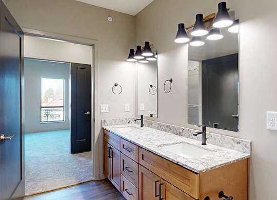 a bathroom with a double vanity sink, two mirrors, and a door to the walk-through closet