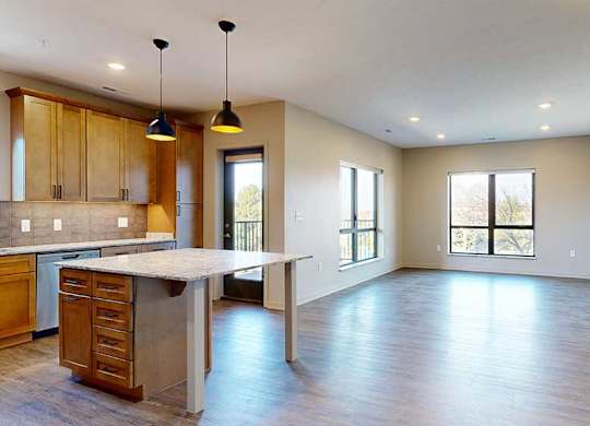 a spacious kitchen with wooden cabinets and a large island next to an open living room with two large windows