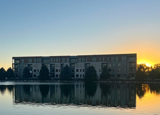 a building on the lake at sunset with the sun setting behind it