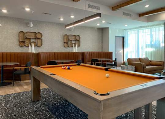 a modern pool table with orange felt in front of some leather seating booths