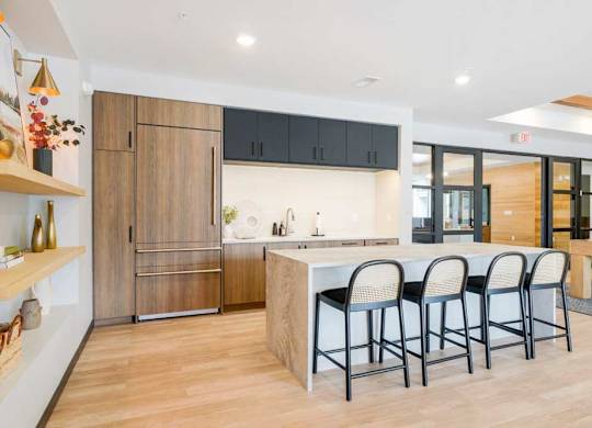 A kitchen in the clubroom with a faux wood fridge, white quartz countertops, and a large island with rattan-back bar stools.