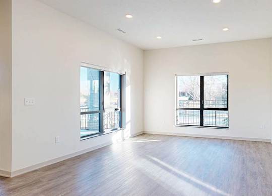 A spacious room with wooden floors and a large window overlooking a balcony.