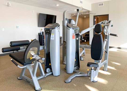 a fitness center with a variety of equipment including a weight machine, a leg press machine, and a rowing machine