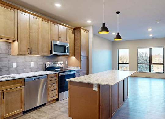 a kitchen with a large central island featuring tan wooden cabinets and light quartz countertops