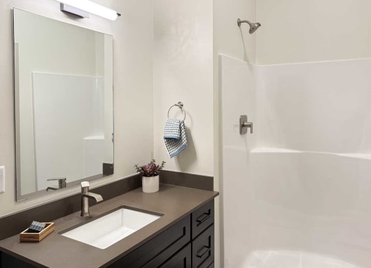 a bathroom with a quartz vanity sink, a mirror with overhead lighting, and a walk-in shower