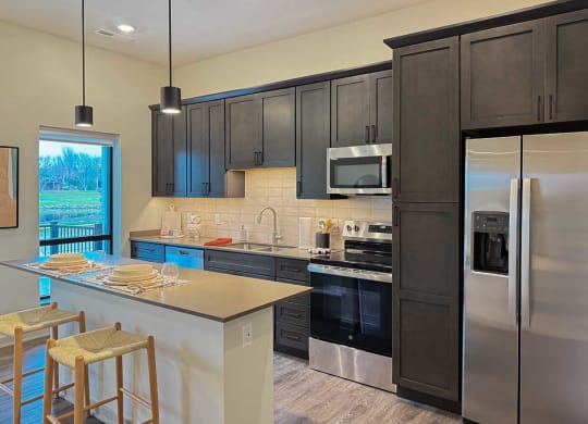 a kitchen with dark cabinets, a tile backsplash, quartz countertops, stainless steel appliances, and a micro-island