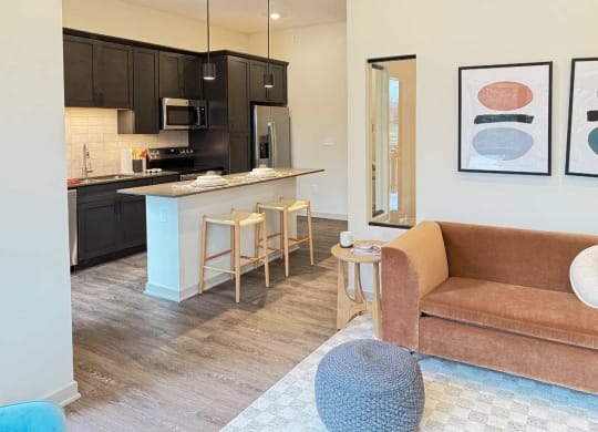 a furnished modern living room next to a spacios kitchen with dark cabinets in the guest suite