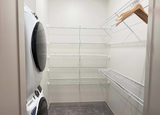 a walk-in closet with built-in shelving and hanging space and a stackable washer and dryer in it