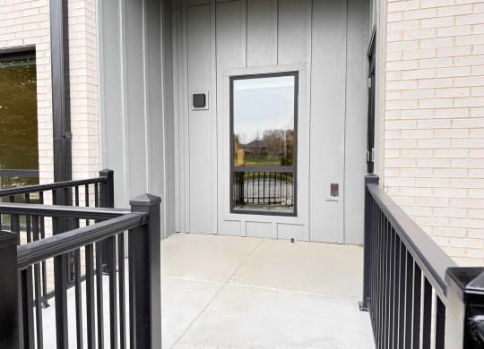 a walk-out patio with black metal railing and a tall window looking into a kitchen