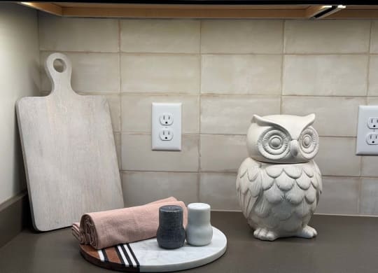 a kitchen countertop decorated with a wooden cutting board, and owl statue, and a serving tray