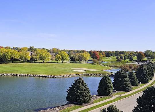a view of a golf course and a pond surrounded by trees