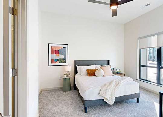 a view of the bedroom from the doorway, furnished with modern decor, a ceiling fan, and a large window overlooking the courtyard