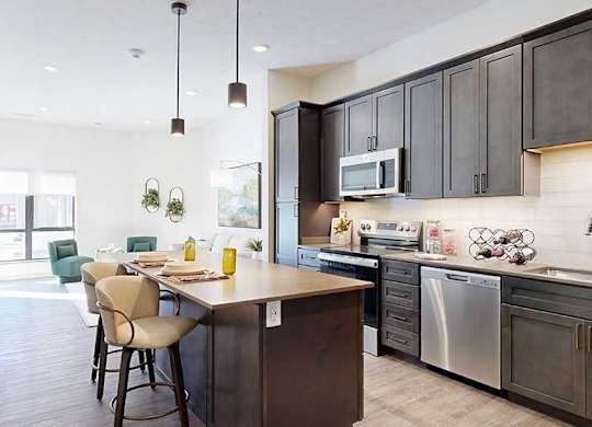 a modern kitchen with a stainless steel appliances, quartz countertops, a light tile backsplash, dark wooden cabinets, and a large central island