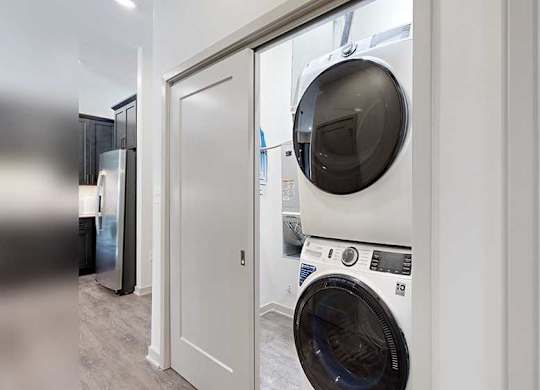 a white and black stackable full-size washer and dryer in a double door closet in the front hallway