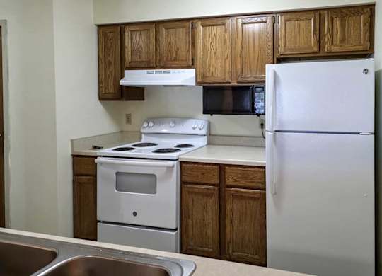 A kitchen with wooden cabinets, white appliances, and a mounted microwave.