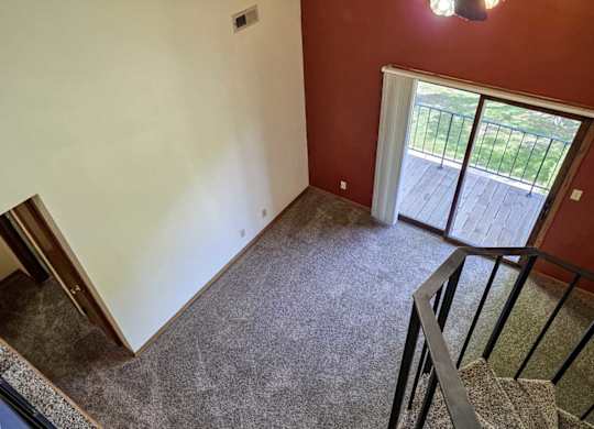 A view of a living room with a red accent wall and a sliding glass door to a balcony, from a loft area.