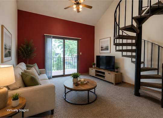 Two-story apartment living room with a loft layout, carpeted flooring, a spiral staircase, ceiling fan, sliding glass door to a private balcony, and a comfortable seating area.