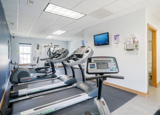 24-hour fitness center with a stationary bike, two treadmills, and an elliptical with a tv on the wall