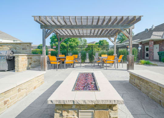 a patio with a fire pit and two stone benches and a pergola
