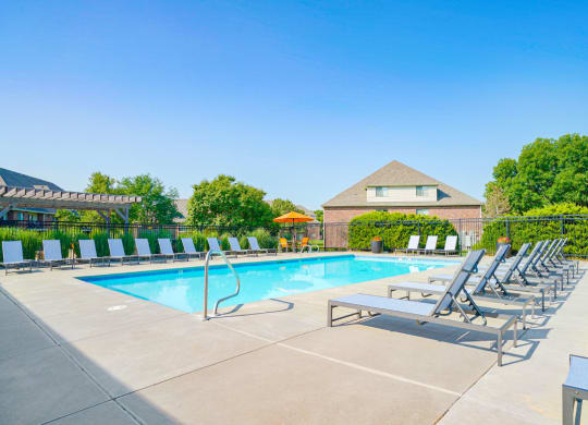 a swimming pool surrounded by rows of lounge chairs with an apartment building in the background