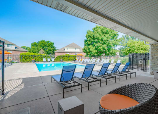 a row of lounge chairs facing the pool under a large awning