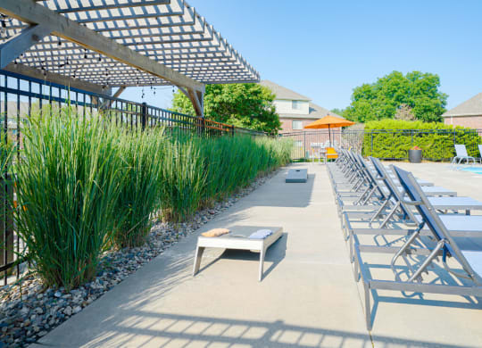 a row of lounge chairs next to a pool with a cornhole game behind it