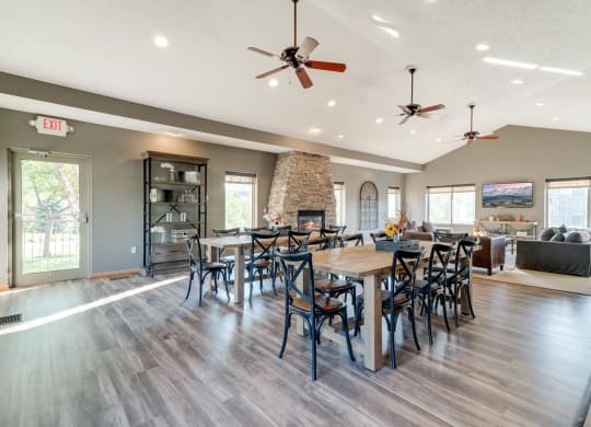 a modern community clubhouse with hardwood floors, large tables, a fireplace, and a tv area
