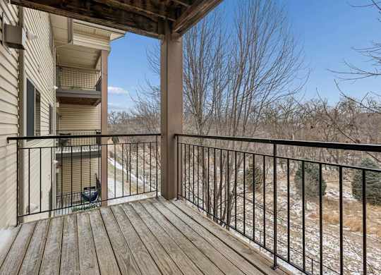 Private apartment balcony with wood decking, metal railing, and views of mature trees, offering an outdoor space accessible from the apartment.