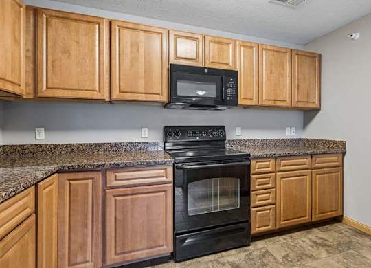 Apartment kitchen with wood cabinets, laminate countertops, black oven and microwave, and ample upper and lower cabinet storage.