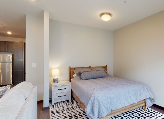 a studio with a bed and bedside table with lamp
