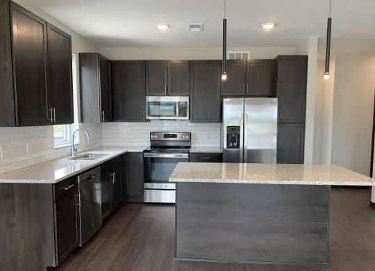 Large kitchen with warm dark brown cabinets, stainless steel appliances, and an island