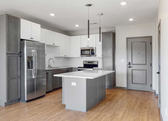 Slate finish kitchen with two tone cabinets, light hard wood style flooring, granite counter tops, and white back splashes in the Bliss floor plan at Haven at Uptown in Lincoln, NE