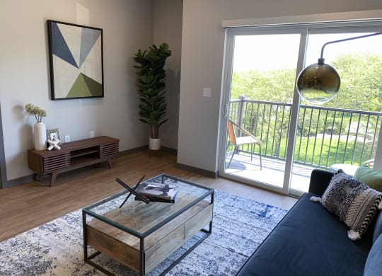 Spacious furnished living room with hard wood style flooring and scenic view of tree line in Lincoln at Haven at Uptown.