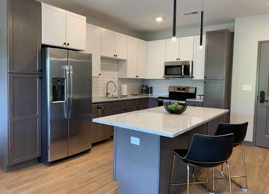 apartment kitchen with stainless steel appliances, white upper cabinets, warm grey lower cabinets, and white counters