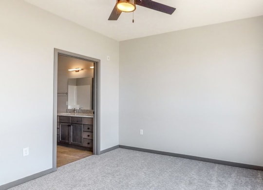 Master bedroom with large windows providing natural light, ceiling fan, and attached bathroom at Haven at Uptown in Lincoln, NE