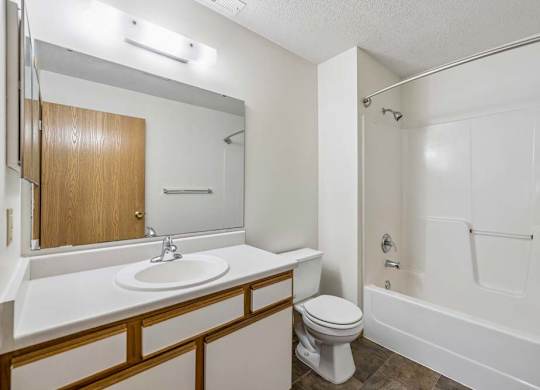 Apartment bathroom with a single-sink vanity, large wall mirror, toilet, and a tub/shower combination with built-in shelving in a bright, neutral interior.