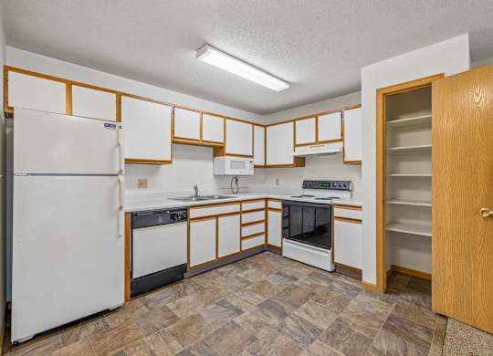 Spacious apartment kitchen with white cabinets, white appliances, a freestanding oven, durable flooring, and a built-in pantry for additional storage.