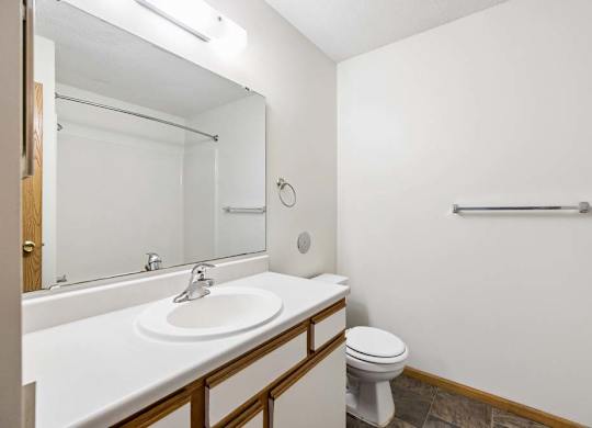 Apartment bathroom with a single-sink vanity, white and wood-tone cabinetry, a large mirror with overhead lighting, and a tub-shower combination with a towel bar.