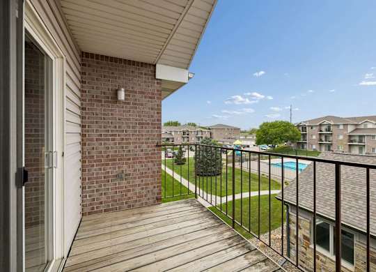 A balcony with a black railing and a brick wall with a pool view.