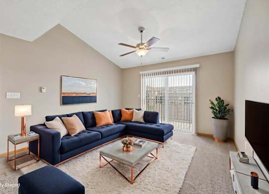 Virtually staged living room with a sectional sofa, coffee table, ceiling fan, large window, and neutral apartment finishes.
