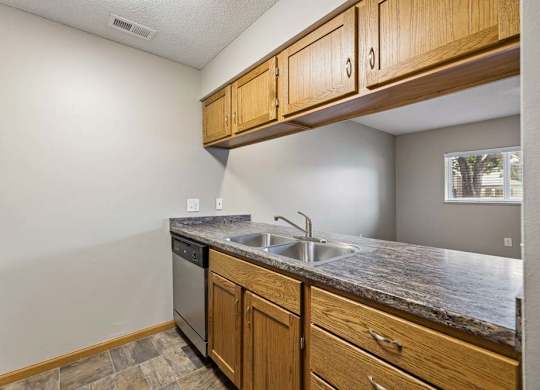Apartment kitchen with wood cabinetry, black appliances, a double-basin sink, laminate countertops, and a pass-through opening connecting to the living area.