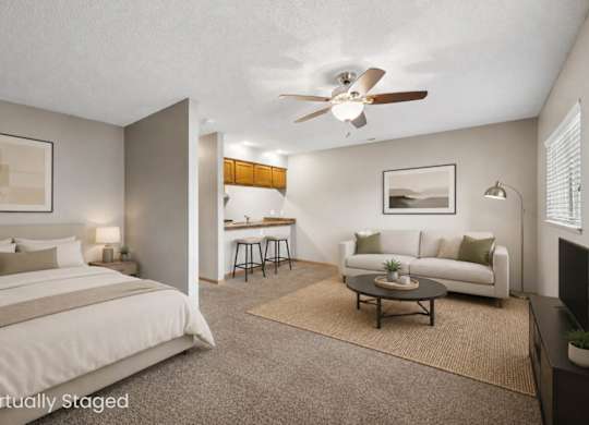 Virtually staged studio apartment featuring a sleeping area, living space, coffee table, ceiling fan, and partial view of the kitchen.
