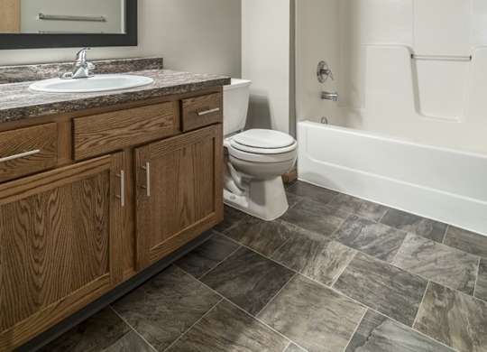 a bathroom with wooden cabinets, a granite vanity sink, a mirror, and a combination shower and tub