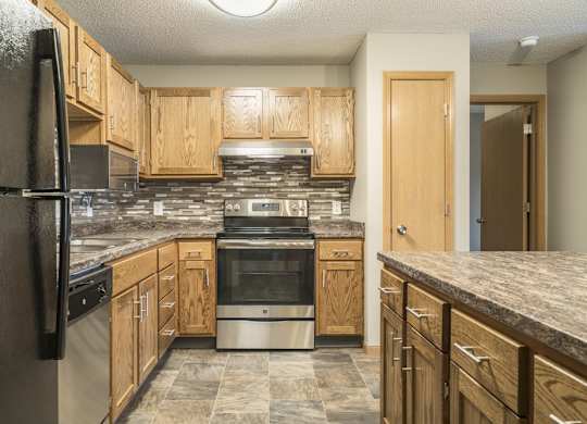 an updated kitchen featuring wooden cabinets, granite countertops, a tile backsplash, stainless steel appliances, and a kitchen island