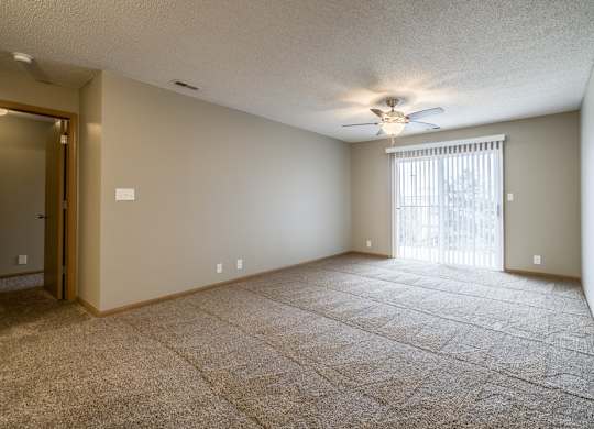 a carpeted living room with a ceiling fan and a sliding glass door to a balcony